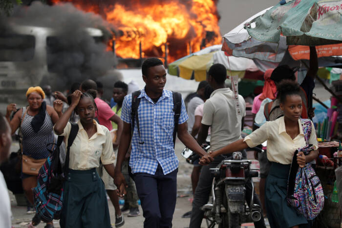 Anak-anak sekolah berjalan di sepanjang jalan saat bus terbakar di latar belakang selama protes yang diselenggarakan oleh "Fantom 509" di jalan-jalan Port-au-Prince, Haiti (REUTERS/Andres Martinez Casares) Anak-anak sekolah berjalan di sepanjang jalan saat bus terbakar di latar belakang selama protes yang diselenggarakan oleh "Fantom 509" di jalan-jalan Port-au-Prince, Haiti