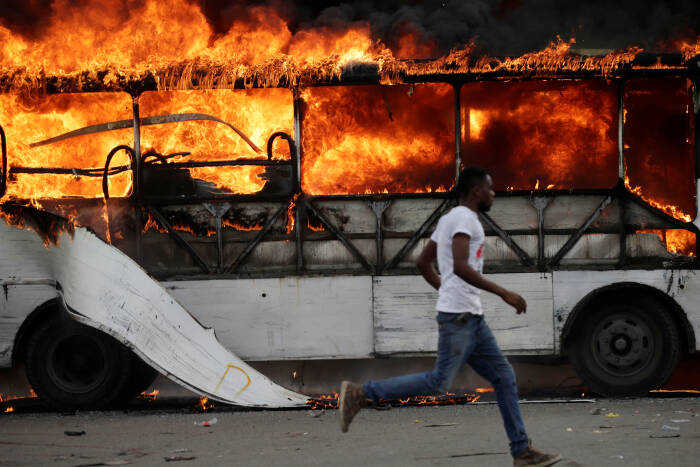 REUTERS/Andres Martinez Casares Seorang pria berlari melewati bus yang terbakar