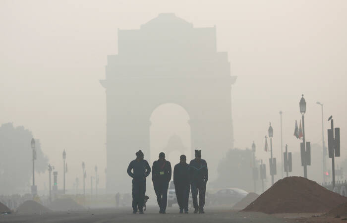 REUTERS/Adnan Abidi Para pria berjalan di depan Gerbang India yang diselimuti kabut asap di New Delhi